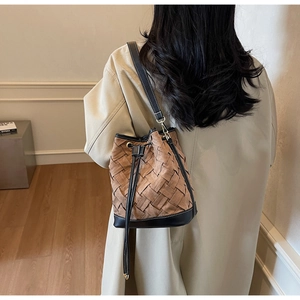 Detail of brown woven bucket bag with black leather trim worn on model's shoulder