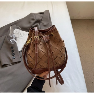 Detail of a brown woven bucket bag featuring suede leather stitching and gold hardware