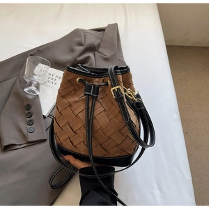 Close-up of woven brown and black bucket bag with drawstring closure and leather strap
