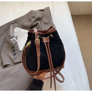 Detail of black woven bucket bag with brown leather trim and gold drawstring hardware