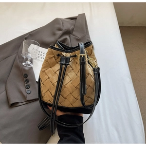 Detail of woven bucket bag featuring contrast trim, drawstring closure and golden hardware