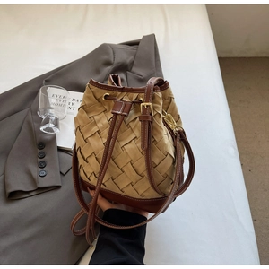 Close-up of woven bucket bag featuring dark brown leather trim and gold metal drawstring