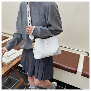 Close-up of white woven bucket bag featuring a patterned shoulder strap and gold hardware