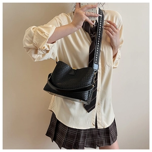 Detail of black woven leather bucket bag featuring a wide geometric patterned shoulder strap