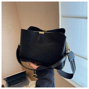 Detail of black woven texture shoulder bag with stylish wide strap and golden hardware