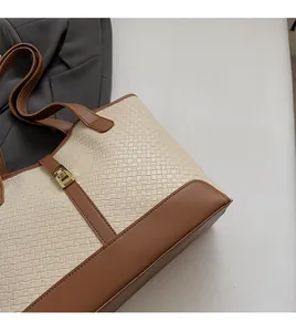 Detailed close-up of woven cream fabric and brown leather tote bag with gold lock