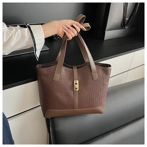 Detail of brown woven tote bag featuring a golden lock and spacious leather design