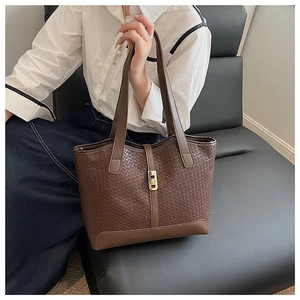 Detail of dark brown tote bag featuring woven texture and gold metal buckle clasp