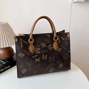 Brown printed tote bag with MYXXING monogram and golden hardware on white desk