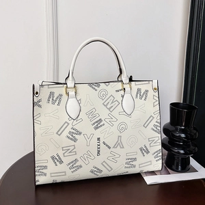 Large white faux leather tote bag with black letter print and golden hardware on wood surface
