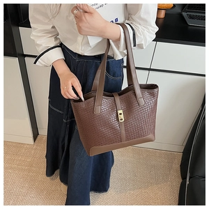 Detail of woven brown tote bag with metal buckle worn by model in casual white shirt