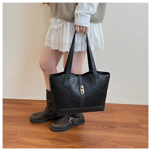 Detail of black woven tote bag featuring gold buckle hardware and premium faux leather texture