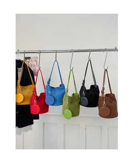 Close-up of minimalist suede bucket bags in six vibrant colors on retail display hooks