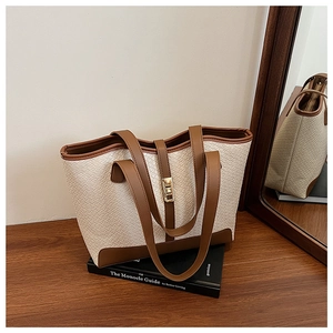 Detail of woven tote bag with brown leather trim and golden square lock on books