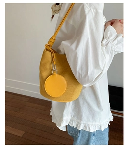 Side view of yellow suede bucket bag with matching round coin pouch on model