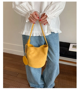 Detail of a vibrant yellow matte bucket bag with long strap shown on a casual outfit