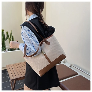 Detail of woven tote bag with brown leather trim and golden metal lock clasp