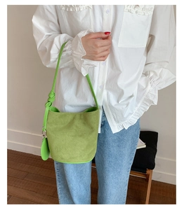 Green suede bucket bag shown on shoulder in a minimalist indoor setting for daily style