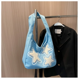 Detail view of light blue tote bag featuring white plush star patches and wide shoulder strap