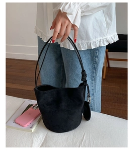 Detail of minimalist black suede bucket bag with slim shoulder strap and round charm