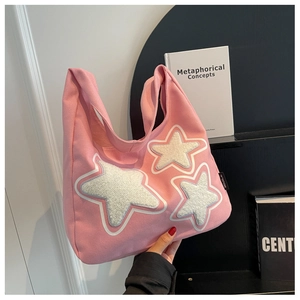 Detail of pink canvas tote bag featuring plush white star patches and side brand label