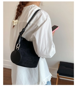 Detail of a black suede bucket bag featuring a detachable round coin purse and leather strap