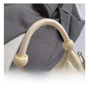 Dettaglio della borsa a mezzaluna crema con manico tondo spesso e grandi perle decorative