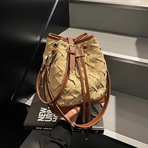 Beige woven bucket bag with brown leather base and adjustable shoulder strap for women