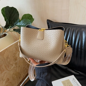 Beige woven leather bucket bag with white embroidered strap in a modern home setting