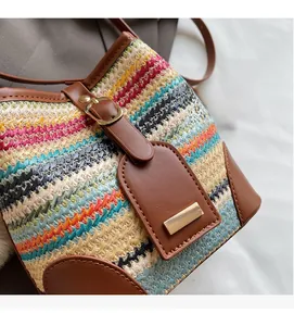 Gros plan du sac seau tissé avec rayures colorées en paille et garniture en cuir brun