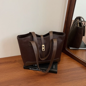 Deep brown woven leather tote bag with gold hardware on a wooden table in an office setting