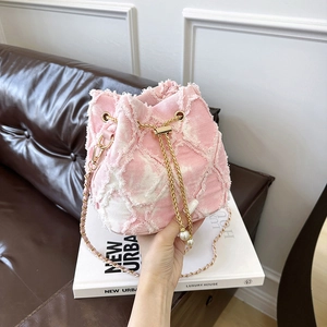 Détail du sac seau en denim rose avec texture florale, chaîne dorée et perle décorative