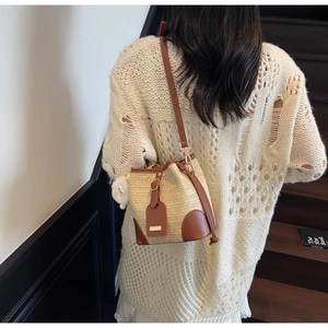 Détail du sac seau en paille avec finitions en cuir et breloque sur un escalier