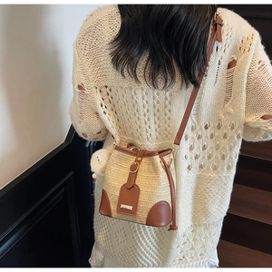 Détail du sac seau en paille tressée avec garniture en cuir brun et breloque peluche