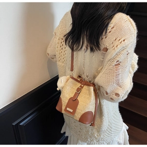 Sac seau en paille avec garniture en cuir marron et pompon porté à l'épaule