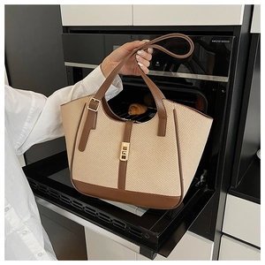 Detail of woven straw tote bag with brown leather trim and metallic turn-lock closure