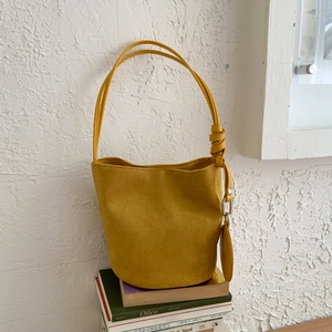 Minimalist yellow suede bucket bag with knotted handle and round coin purse on white books