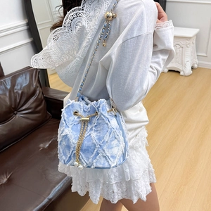 Détail du sac seau en denim bleu clair avec bords effilochés et cordon doré perlé