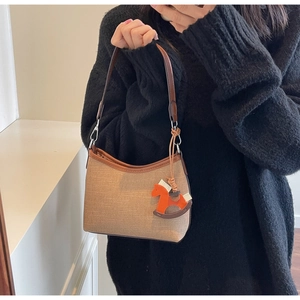 Detail of woven light brown handbag with dark leather trim and orange horse charm