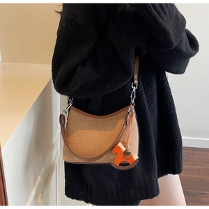 Detail of canvas shoulder bag with brown leather trim and a cute orange horse charm