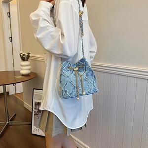 Détail du sac seau en denim bleu clair avec texture matelassée et cordon perlé
