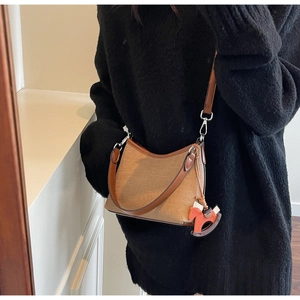 Detail of tan canvas shoulder bag with leather trim and decorative horse charm accessory