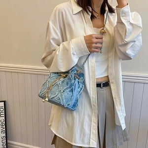 Détail du sac seau en jean bleu clair avec franges, breloques perles et bandoulière