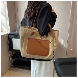 Detailed shot of beige canvas tote bag with brown leather handles worn by a model