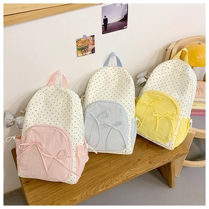 Bow detail on polka dot backpacks in pink, blue, and yellow colors on a wooden bench
