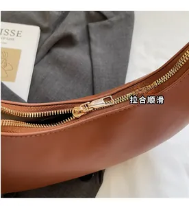 Close-up of golden metal zipper detail on brown leather crescent bag with smooth finish