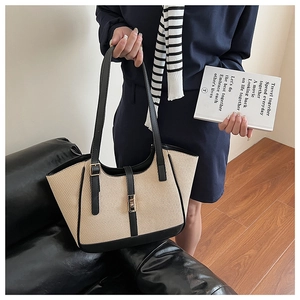 Close-up of woven tote bag featuring black leather trim and golden metal lock detail