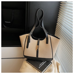 Detail of woven tote bag with black leather trim and elegant golden metal buckle closure