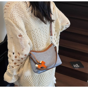 Detail of light blue textured shoulder bag with brown leather trim and orange horse charm