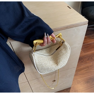 Detail of cream straw woven crescent bag with gold curved handle and chain strap